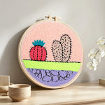 Whimsical cactus and cracked earth punch needle artwork displayed on a table