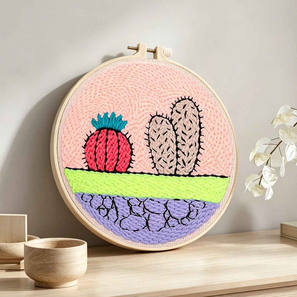 Whimsical cactus and cracked earth punch needle artwork displayed on a table