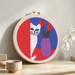 White cat and purple vase punch needle artwork displayed on a table