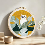 White cat in green leaves punch needle artwork displayed on a table