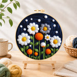 Finished white flowers and orange orbs on navy needle felting displayed on a wooden easel