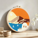 White house by blue sea under orange sky punch needle artwork displayed on a table