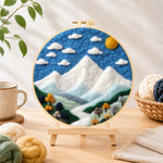 Finished white mountain peaks under the blue sky needle felting displayed on a wooden easel