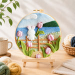 Finished white rabbit on fence with tulips needle felting displayed on a wooden easel