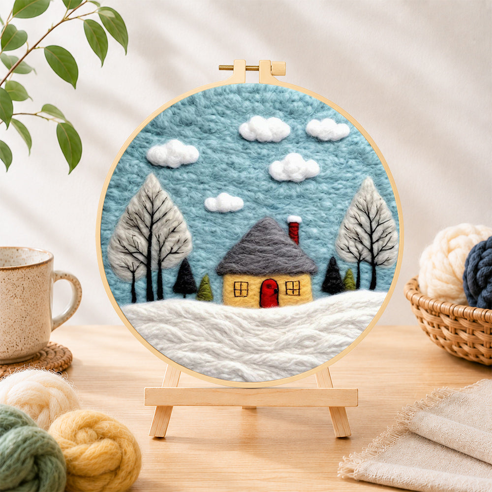 Finished winter cabin and snow-covered trees needle felting displayed on a wooden easel