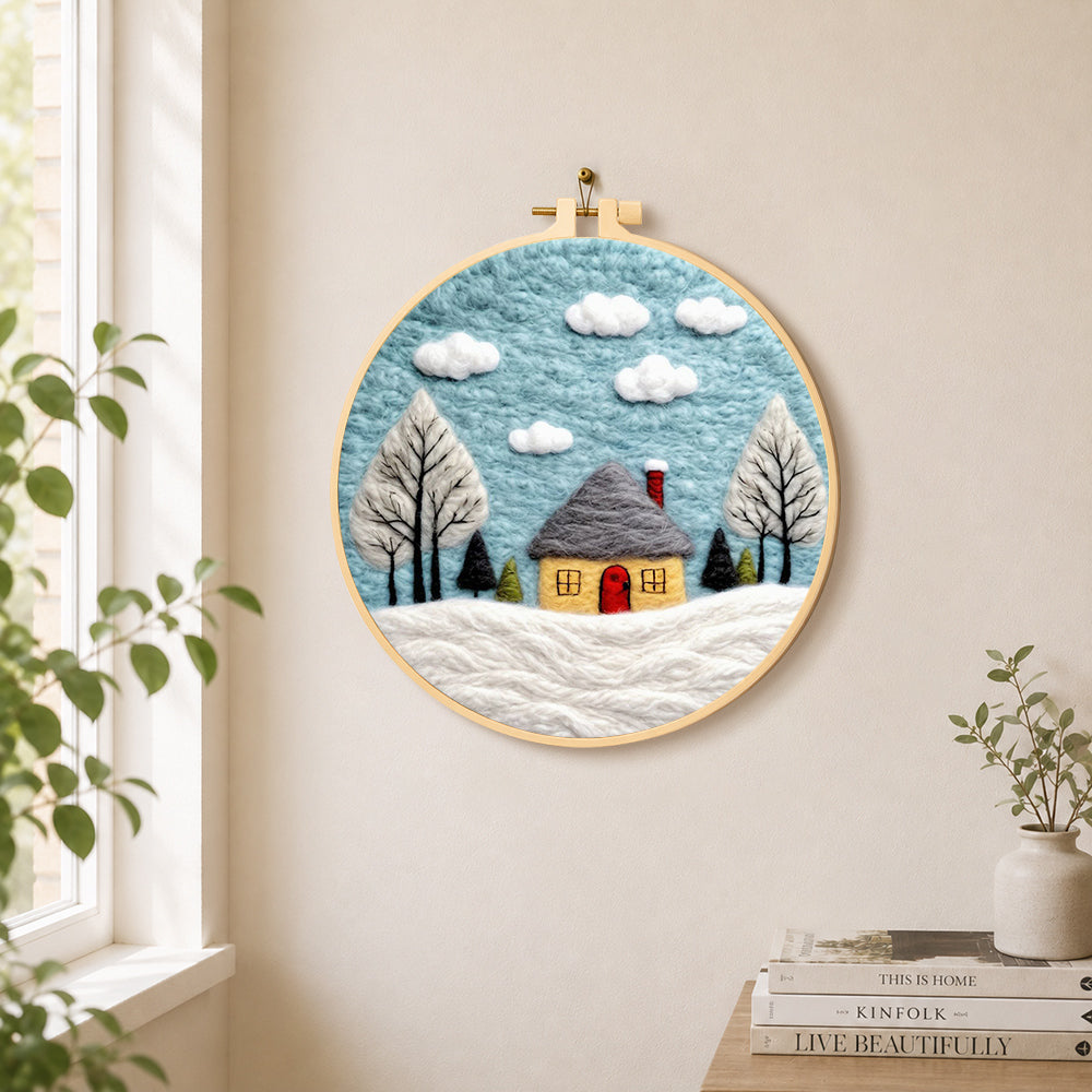 Winter cabin and snow-covered trees needle felt wall art displayed in a bright home interior