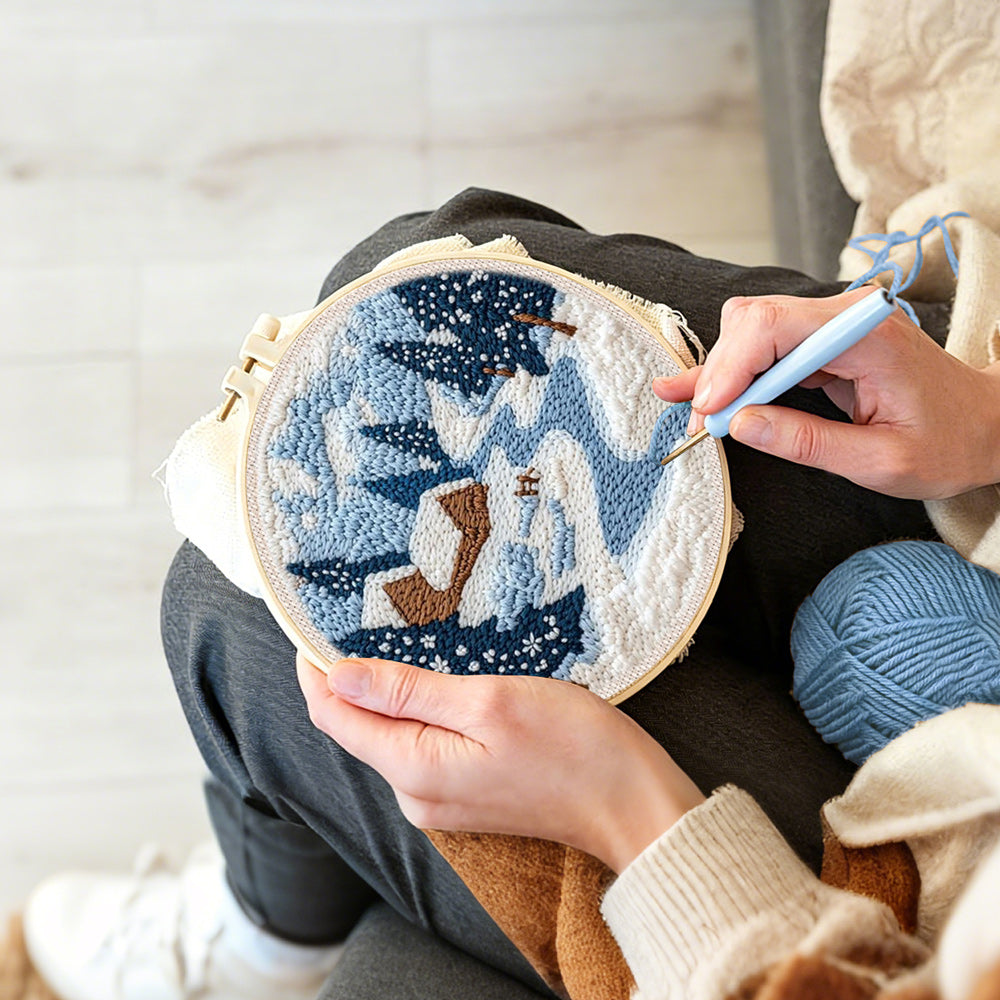 Creating handmade winter cabin scene with snowy pine trees and blue river punch needle artwork