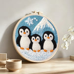 Winter penguin family and mountain punch needle artwork displayed on a table