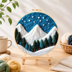 Finished winter snowy peaks and pine forest needle felting displayed on a wooden easel