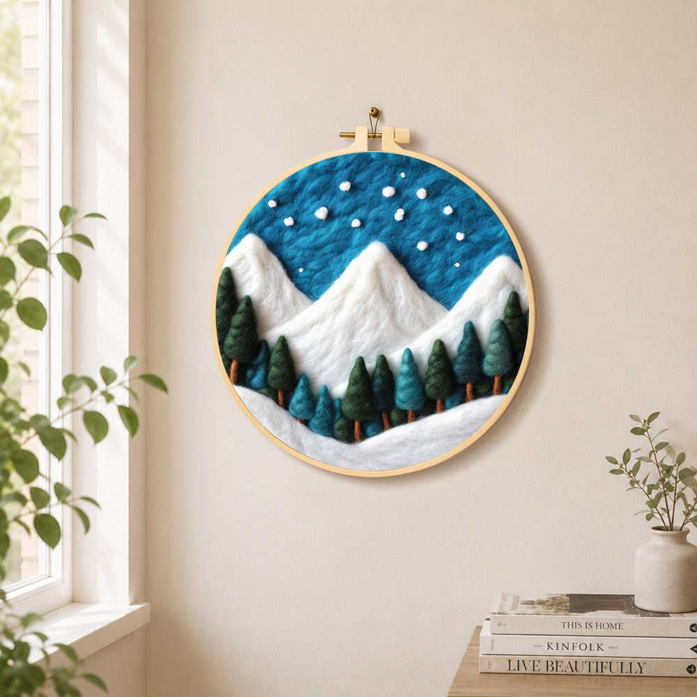 Winter snowy peaks and pine forest needle felt wall art displayed in a bright home interior