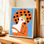 Woman with red lips in orange punch needle artwork displayed on a table