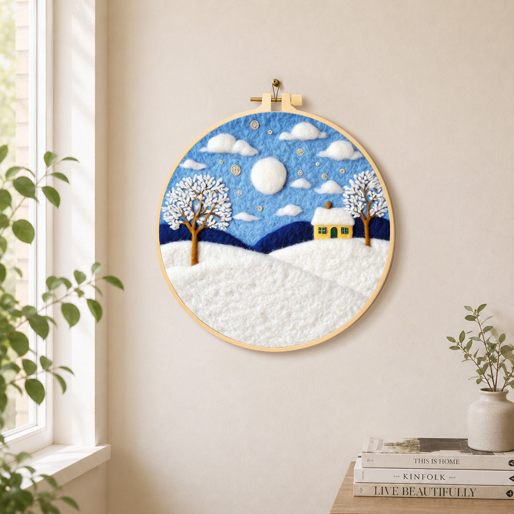 Yellow cottage in the snow needle felt wall art displayed in a bright home interior