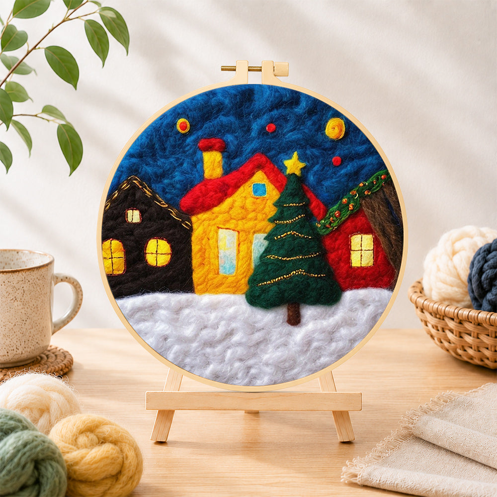 Finished yellow house and christmas tree in snowy village needle felting displayed on a wooden easel