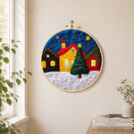 Yellow house and christmas tree in snowy village needle felt wall art displayed in a bright home interior