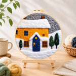 Finished yellow house and snowy ground needle felting displayed on a wooden easel