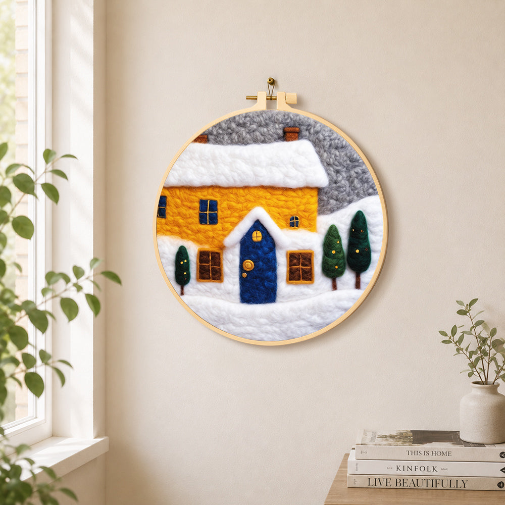 Yellow house and snowy ground needle felt wall art displayed in a bright home interior