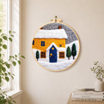 Yellow house and snowy ground needle felt wall art displayed in a bright home interior