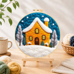 Finished yellow house glowing in the blue snowy night needle felting displayed on a wooden easel