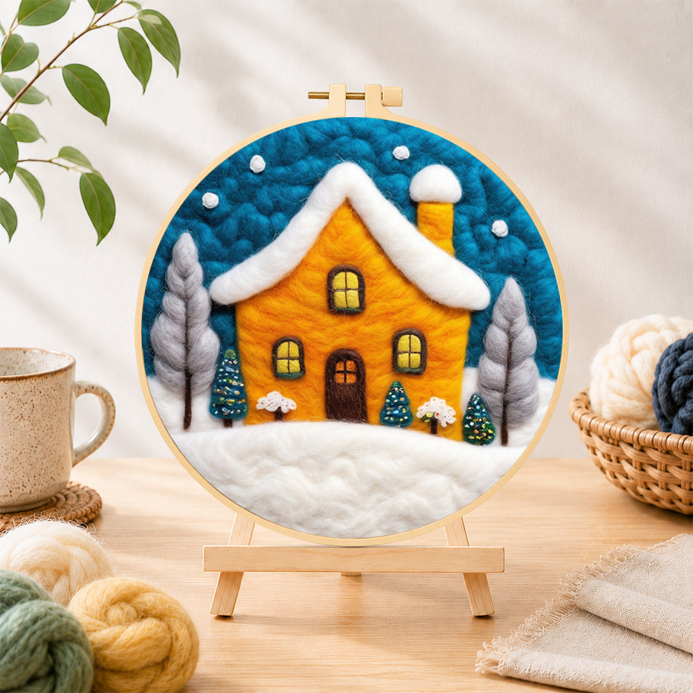 Finished yellow house glowing in the blue snowy night needle felting displayed on a wooden easel