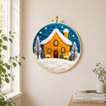 Yellow house glowing in the blue snowy night needle felt wall art displayed in a bright home interior