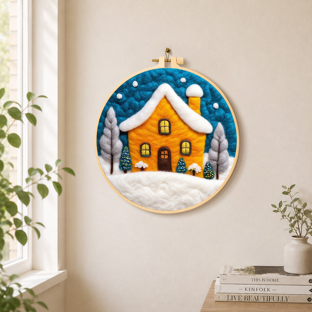 Yellow house glowing in the blue snowy night needle felt wall art displayed in a bright home interior