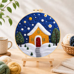 Finished yellow house with snowy path needle felting displayed on a wooden easel