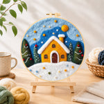 Finished yellow snowy cottage at christmas needle felting displayed on a wooden easel