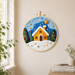 Yellow snowy cottage at christmas needle felt wall art displayed in a bright home interior