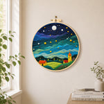 Yellow tower house and rolling green clouds needle felt wall art displayed in a bright home interior