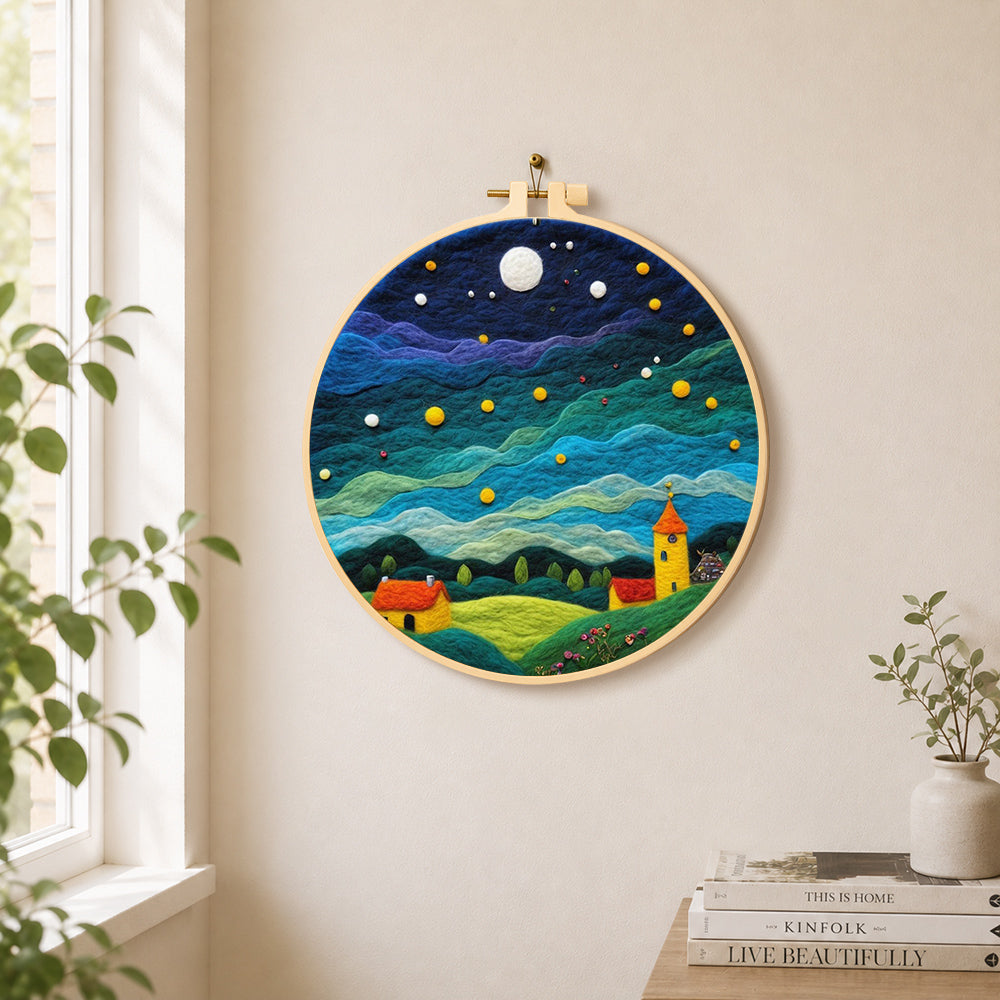 Yellow tower house and rolling green clouds needle felt wall art displayed in a bright home interior
